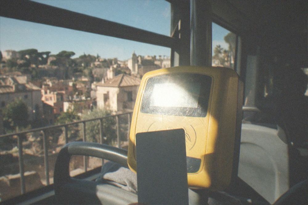A hand holding a contactless bank card near a yellow validator on a Rome bus