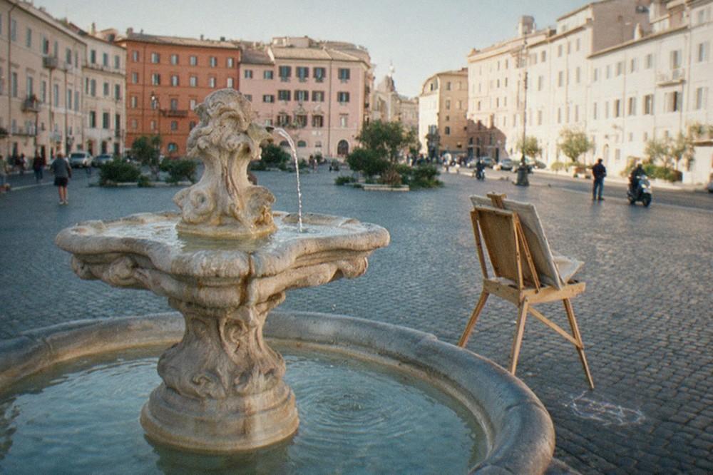 A cobblestone Roman square with an ornate fountain and pastel facades in morning light