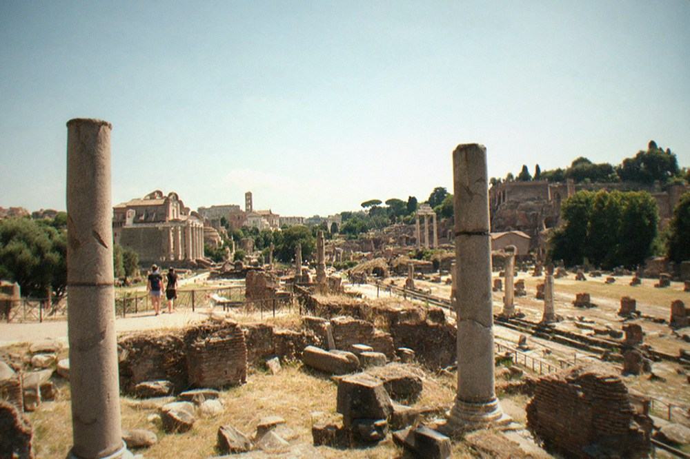 Ancient stone columns and ruined walls of a Roman forum under a wide sky