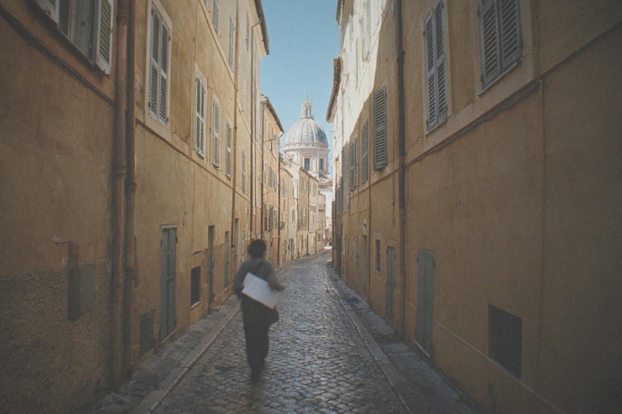A narrow Rome street with ochre buildings and a distant dome under a clear sky