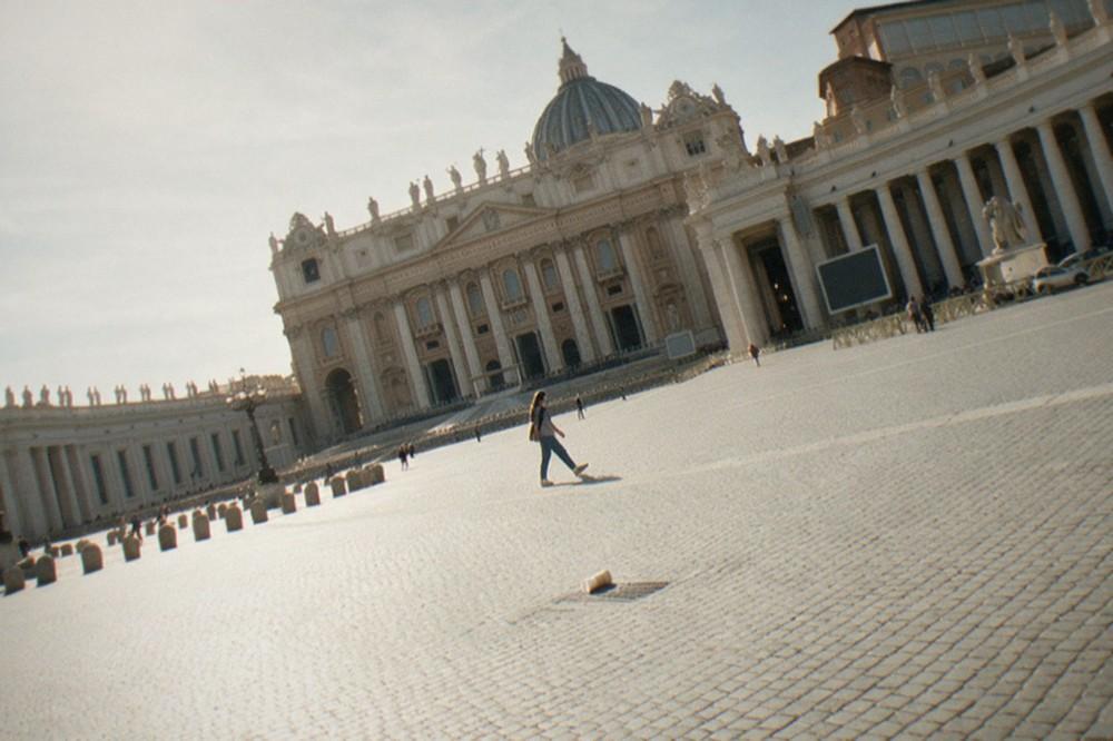 Wide stone square with rows of columns framing a church facade in morning light
