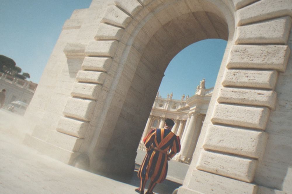 Uniformed guard standing beside a stone archway in bright daylight