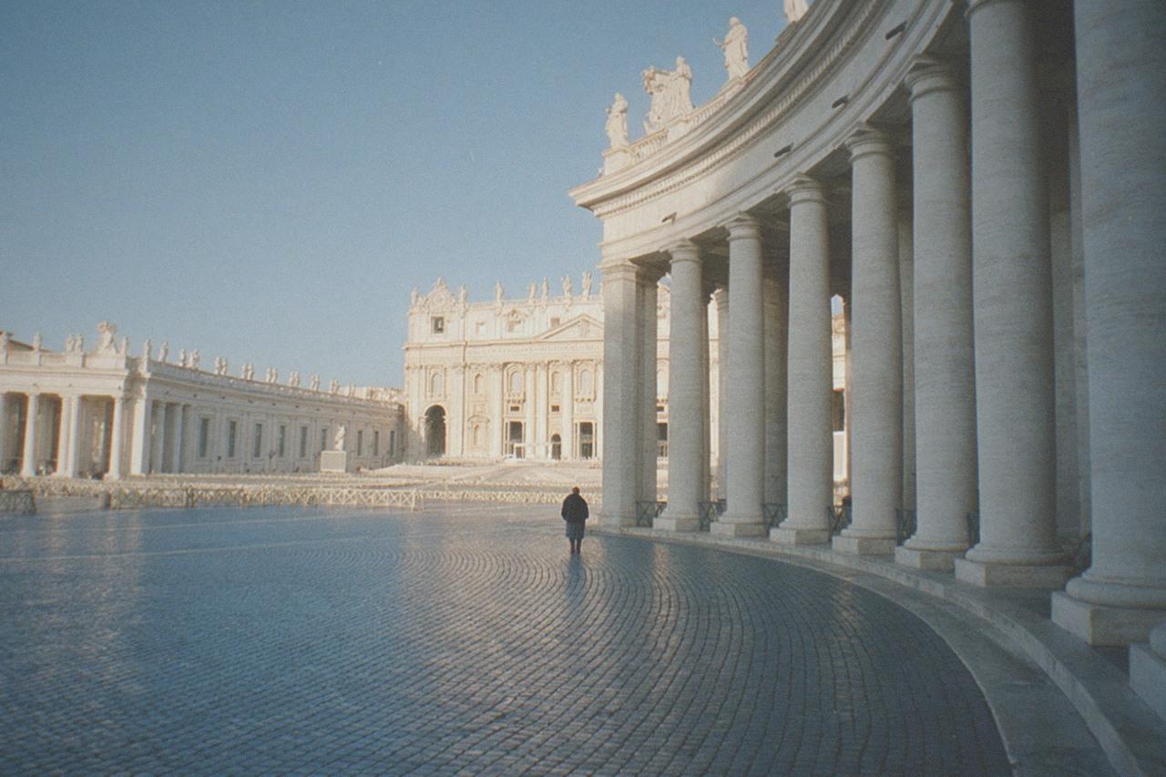 Stone colonnade of St Peter's Square opening onto the basilica facade under a clear sky