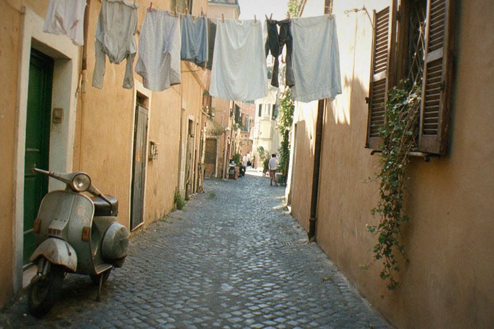 Narrow Roman street with laundry hanging between ochre walls and a scooter parked by a doorway