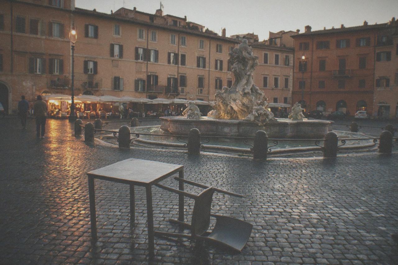 Cobbled Roman square with a stone fountain and ochre apartment buildings at dusk