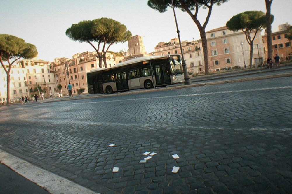 A city bus at a stop on a tree-lined Roman street in late afternoon light