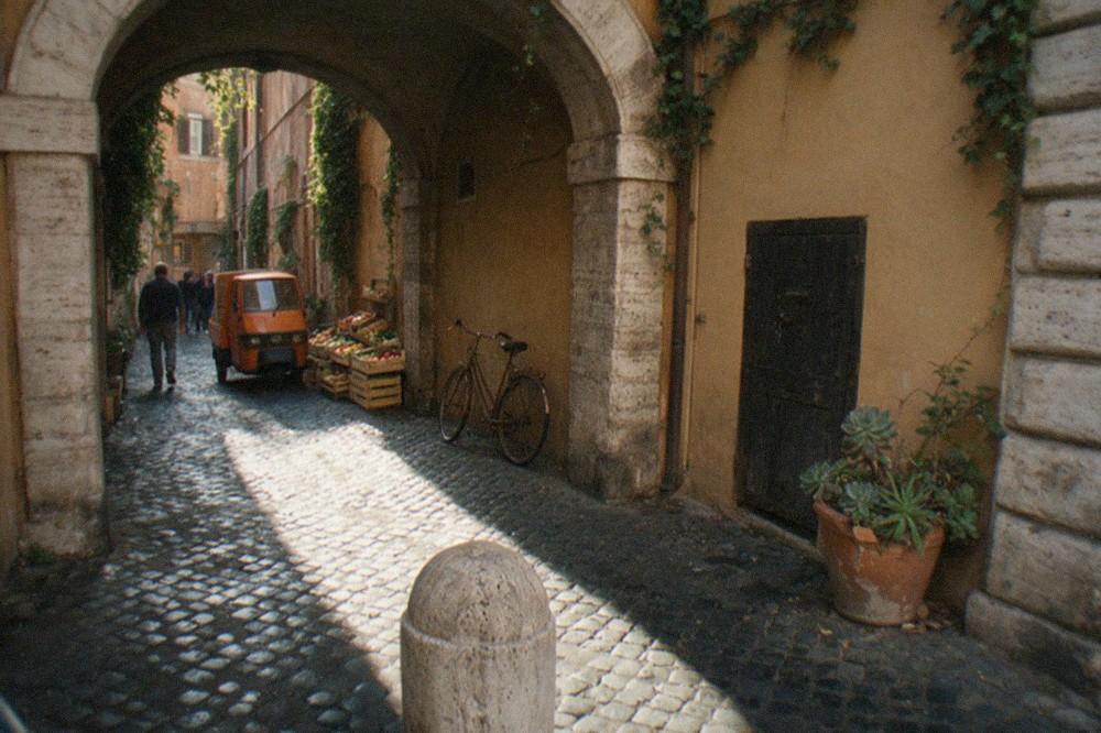 A narrow Roman alley with ivy on ochre walls and a stone archway