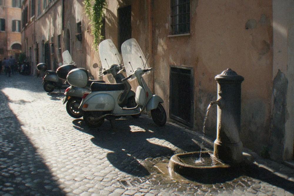 A narrow Rome street with ochre buildings, parked scooters and morning shadows
