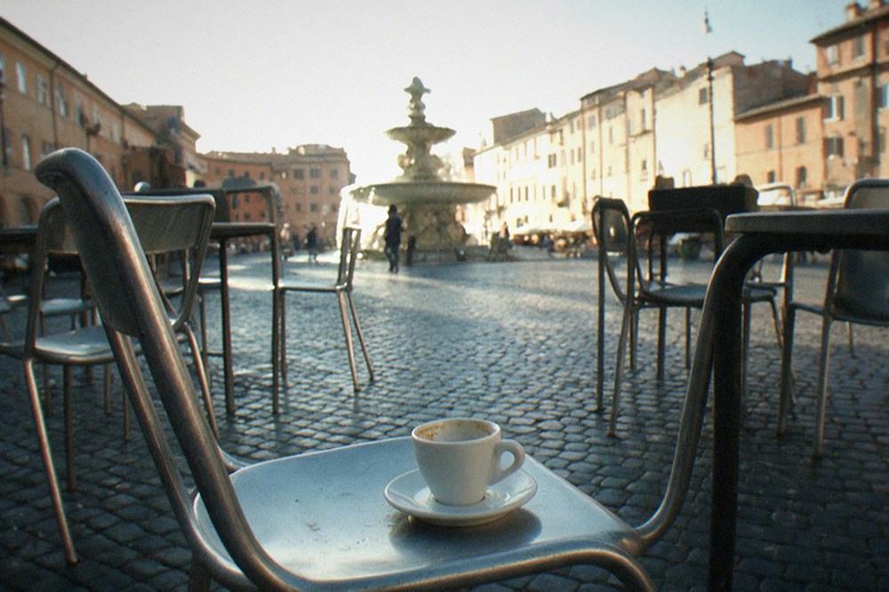 A stone piazza in Rome with a fountain and cafe tables in soft daylight