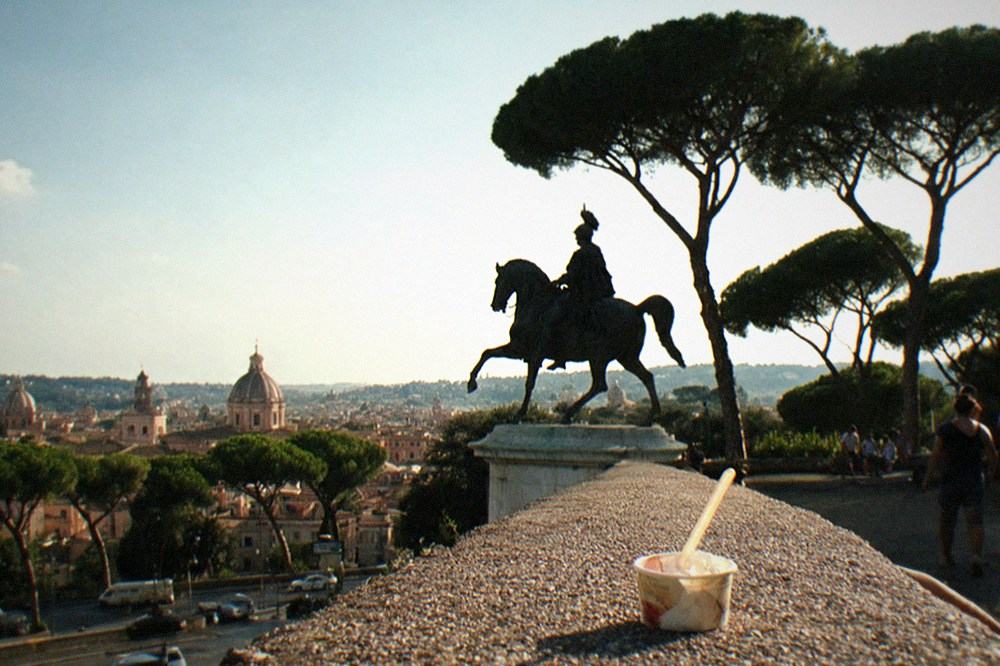Silhouette of umbrella pines and a statue on the Gianicolo hill with the city glowing golden behind