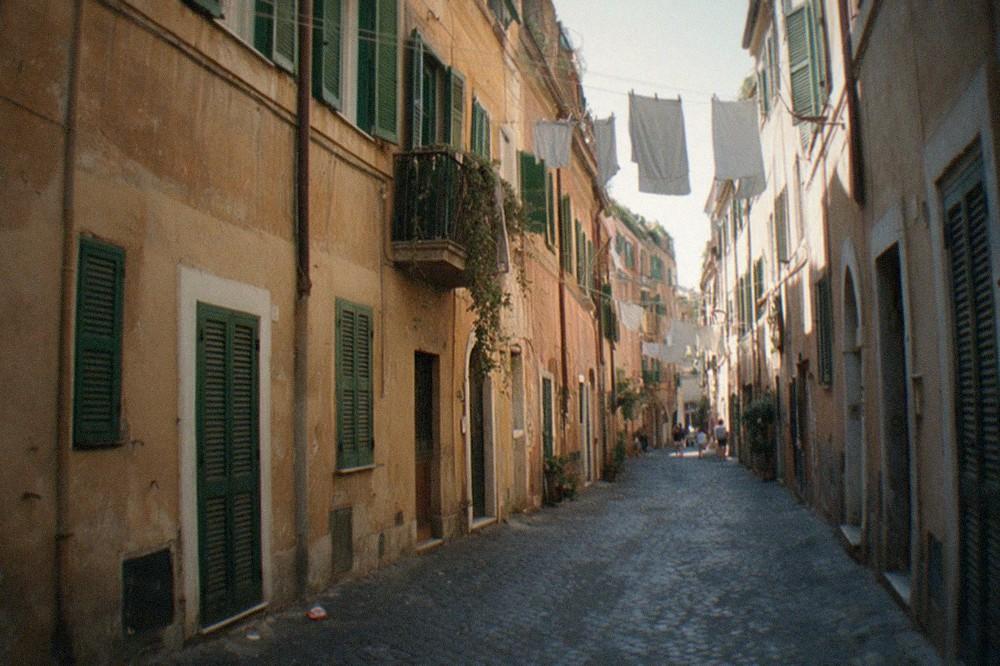 A narrow cobblestone Roman street with ochre buildings and shuttered windows