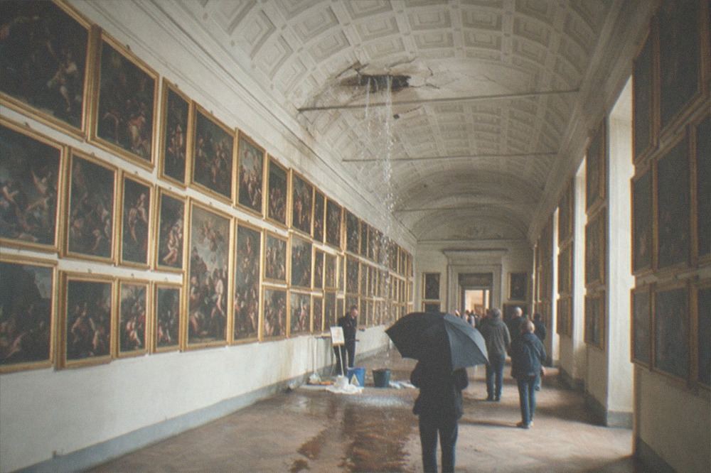 Gallery hall with framed baroque paintings hung in rows under a coffered ceiling