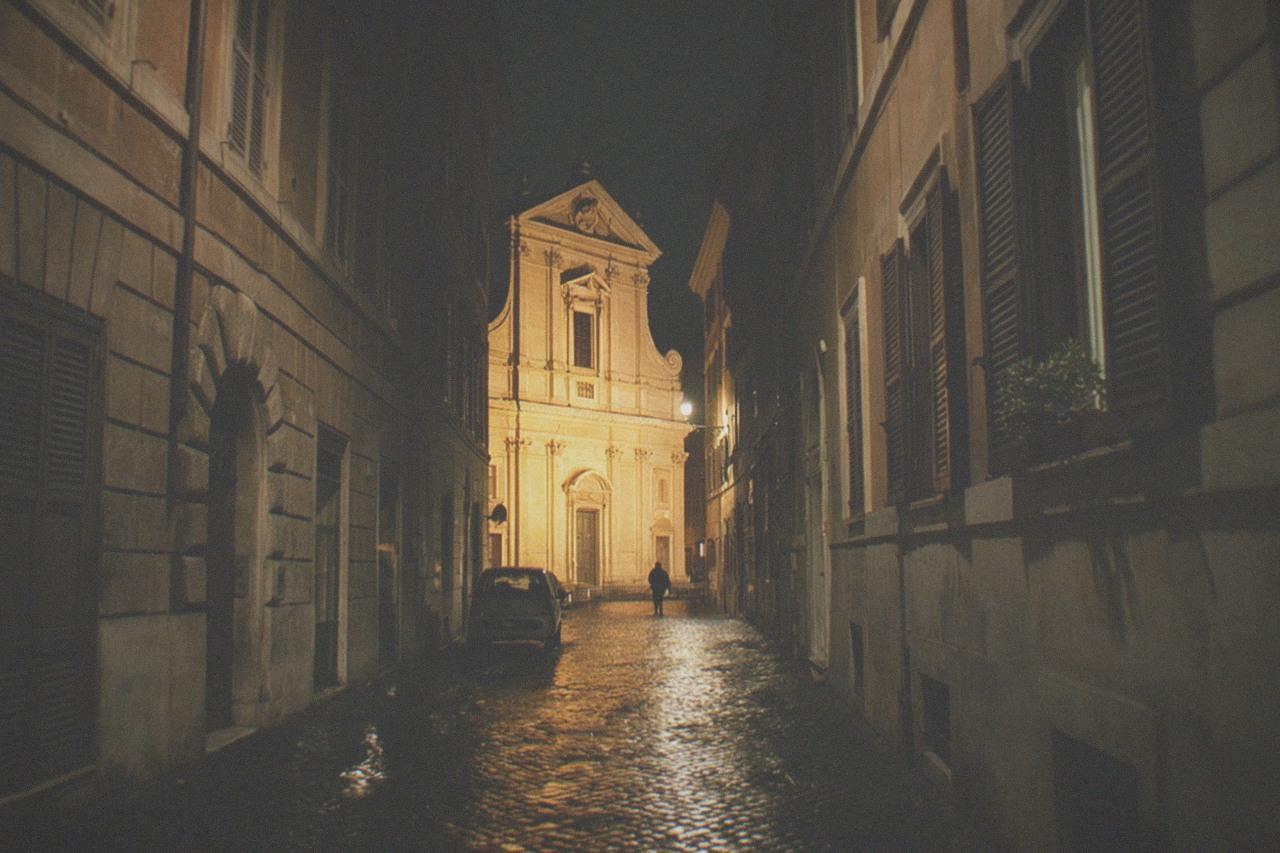 Empty Rome street at night with lit baroque facade and wet cobblestones