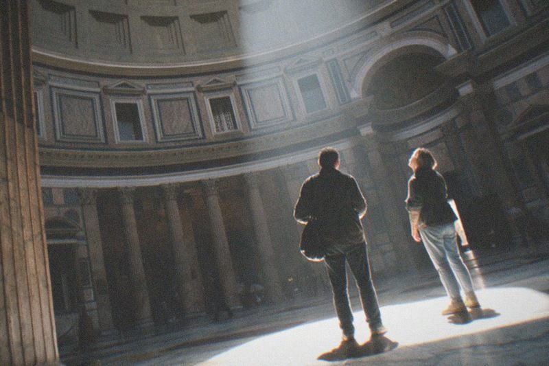 Afternoon light rakes down through the coffered dome of the Pantheon onto its worn marble floor, Corinthian columns standing in the shadowed rotunda.