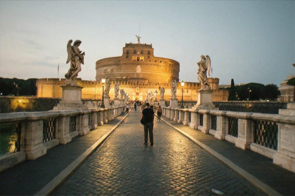 Ponte Sant'Angelo at dusk with the ten angel statues lined along the balustrade and Castel Sant'Angelo lit up in the background, the Tiber reflecting the golden light.