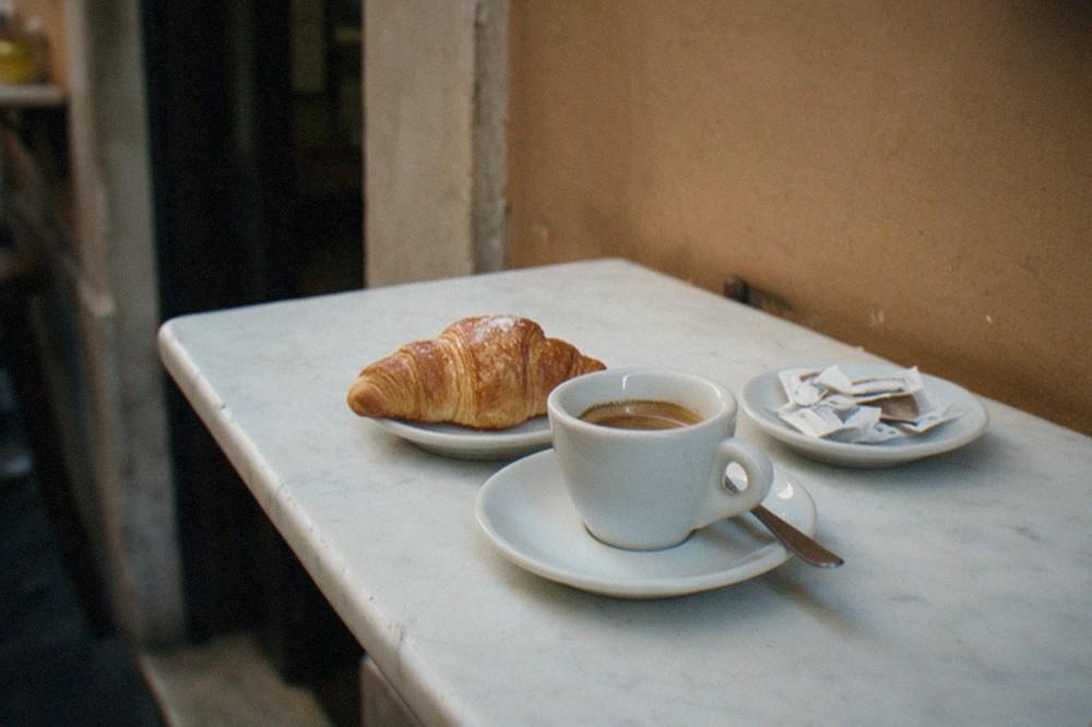A marble bar counter in a Roman cafe with an espresso cup and a pastry on a plate