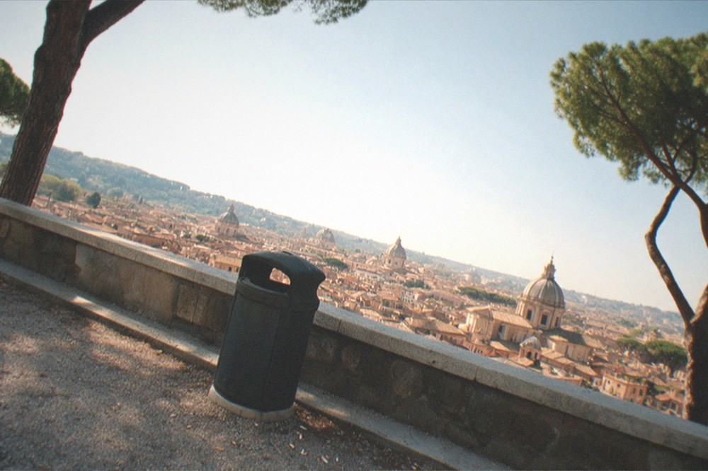 A panoramic view over Rome rooftops and domes from a green hillside terrace