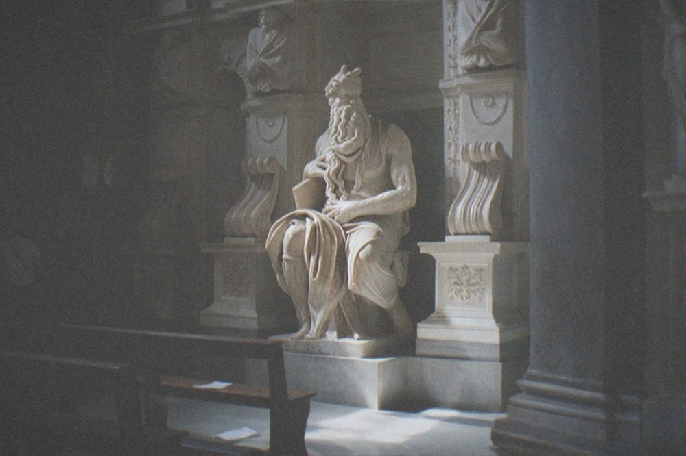 Marble statue of Moses with horns holding stone tablets inside a dim church