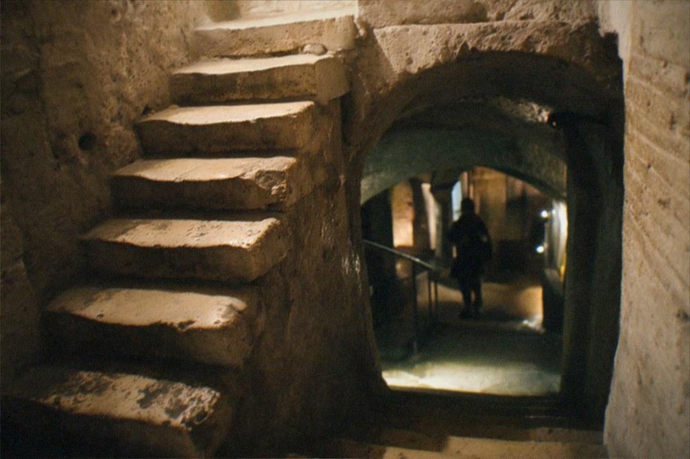Ancient stone staircase descending into an underground crypt lit by lamps
