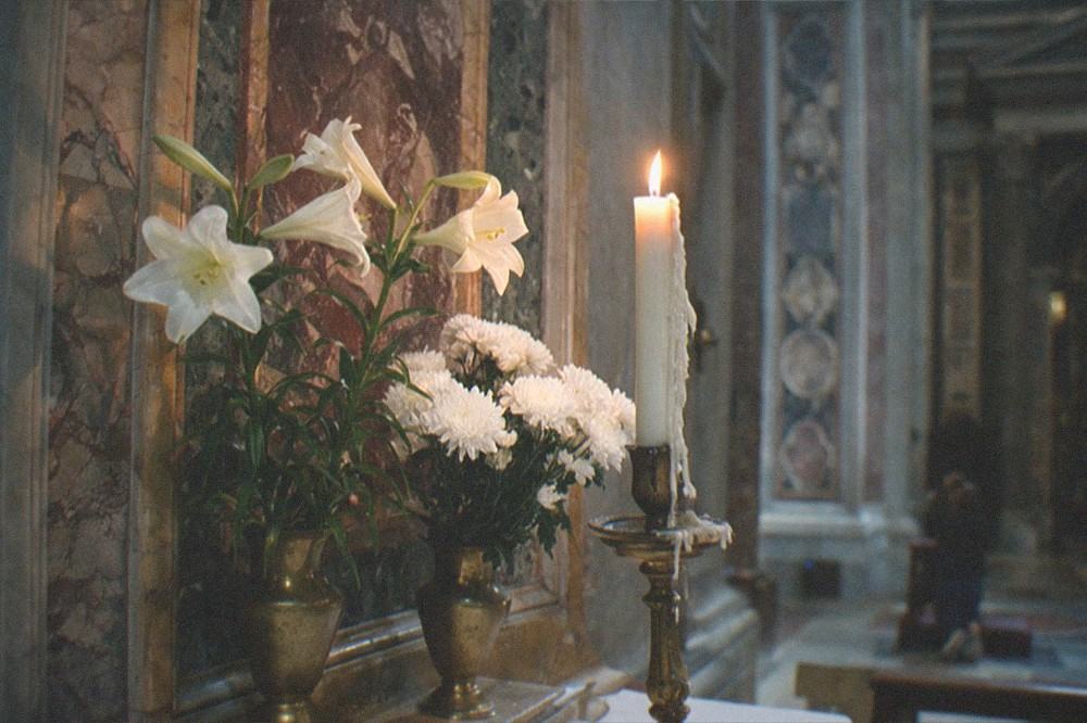 Candlelit side altar with fresh flowers inside a quiet Roman church