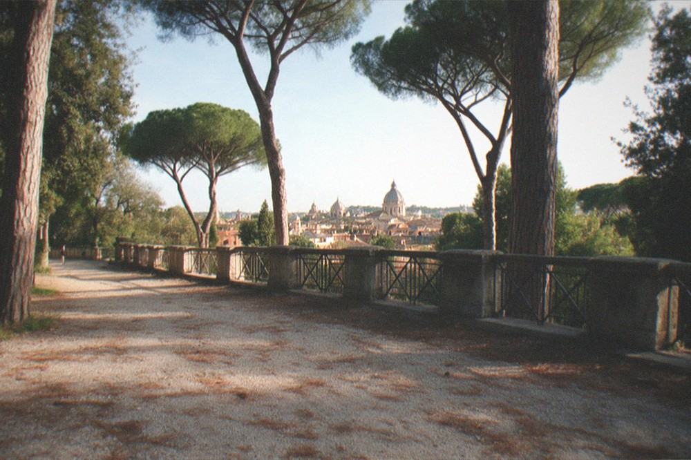 A tree-lined Rome viewpoint overlooking rooftops and domes