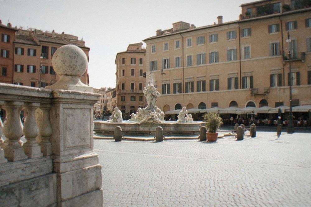 A wide Roman square at golden hour with fountain and facades