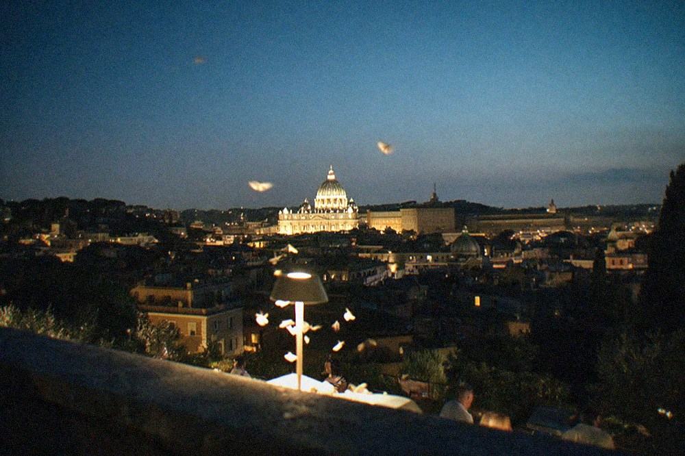 Rooftops and dome of St Peter's lit at night seen from a hilltop terrace
