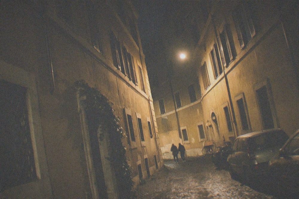 Narrow cobbled Roman street lit by lamps at night with old facades