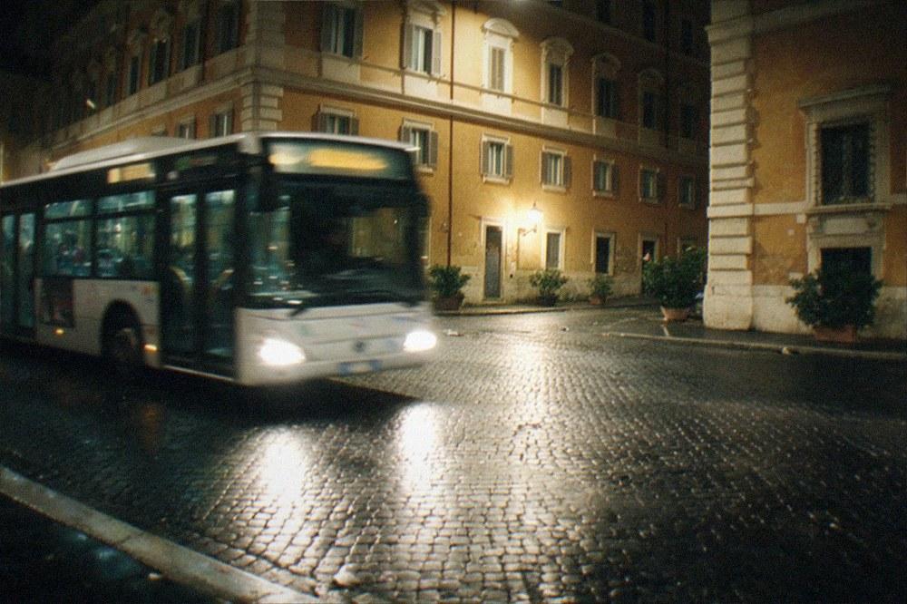 Illuminated Rome street at night with a bus passing lit classical buildings
