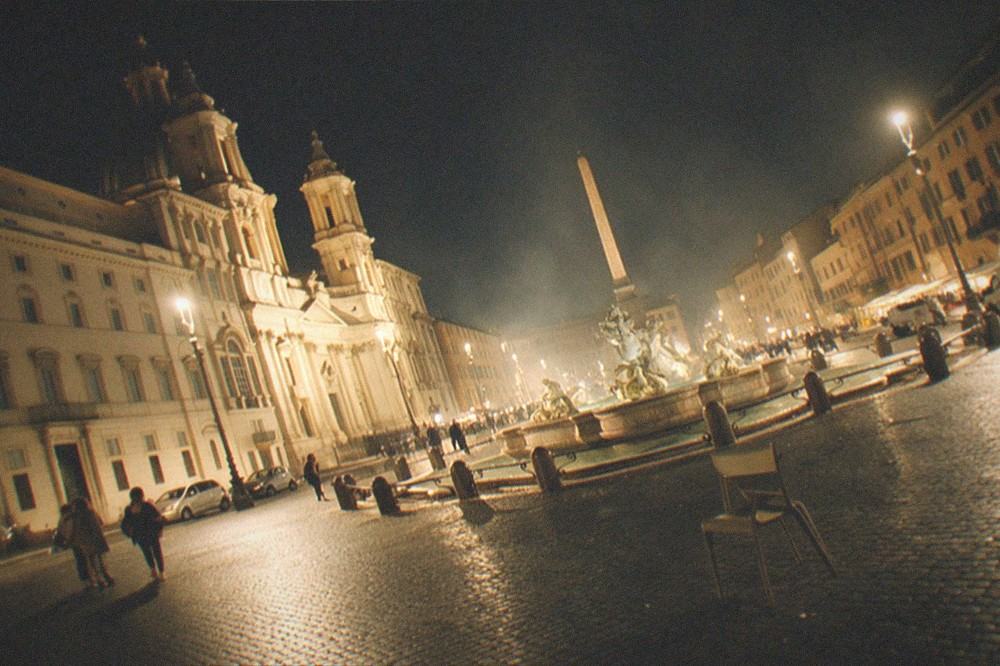 Lit city street in Rome at night with people walking and buildings glowing