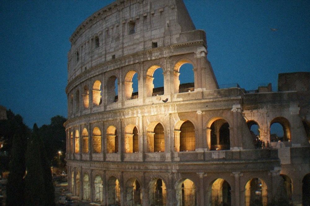 Ancient Roman monument lit by floodlights against a dark evening sky