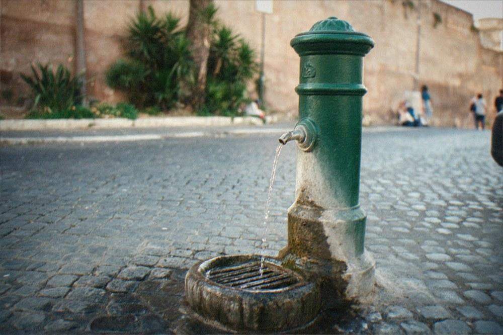 A cast-iron drinking fountain with a constant trickle of water on a Roman street corner