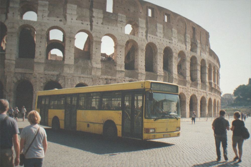 Yellow ATAC bus moving along a Rome street with the Colosseum in the background.