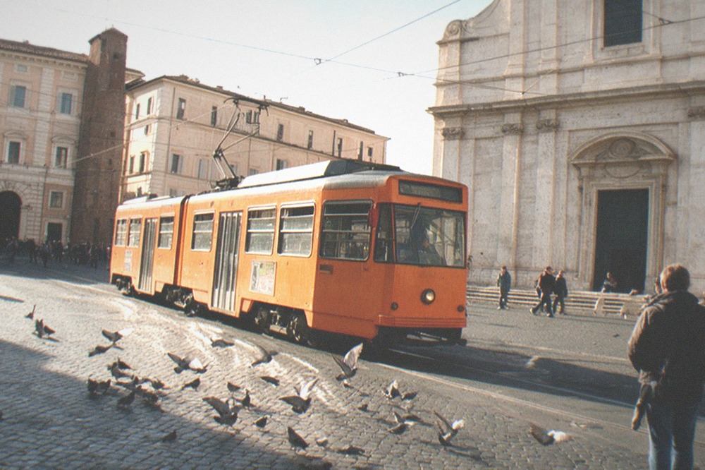Rome tram on tracks passing by an old church in a bustling square.