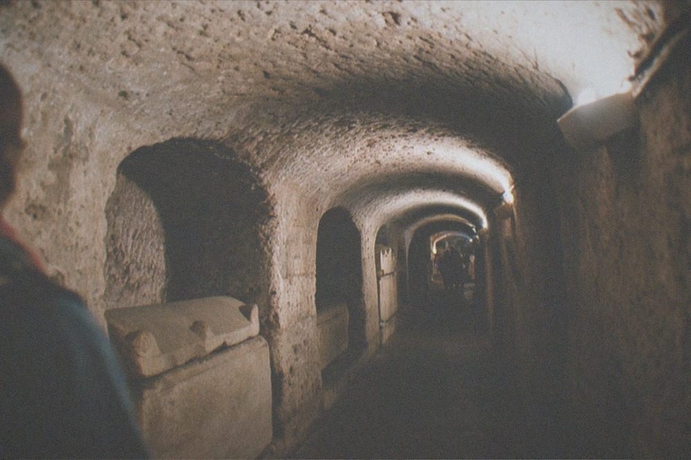 Low vaulted stone corridor of the Vatican Grottoes with sarcophagi along the walls