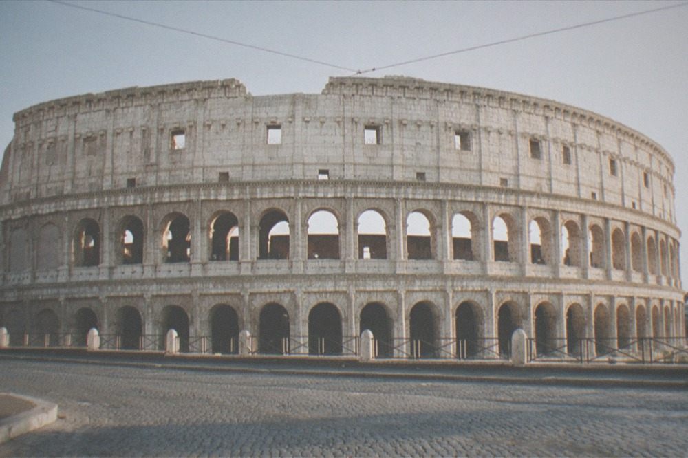 The exterior arches of the Colosseum seen from a cobbled street in late afternoon light
