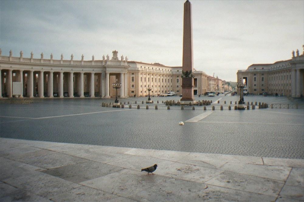 A wide stone square with an obelisk at its centre and colonnades curving around the sides