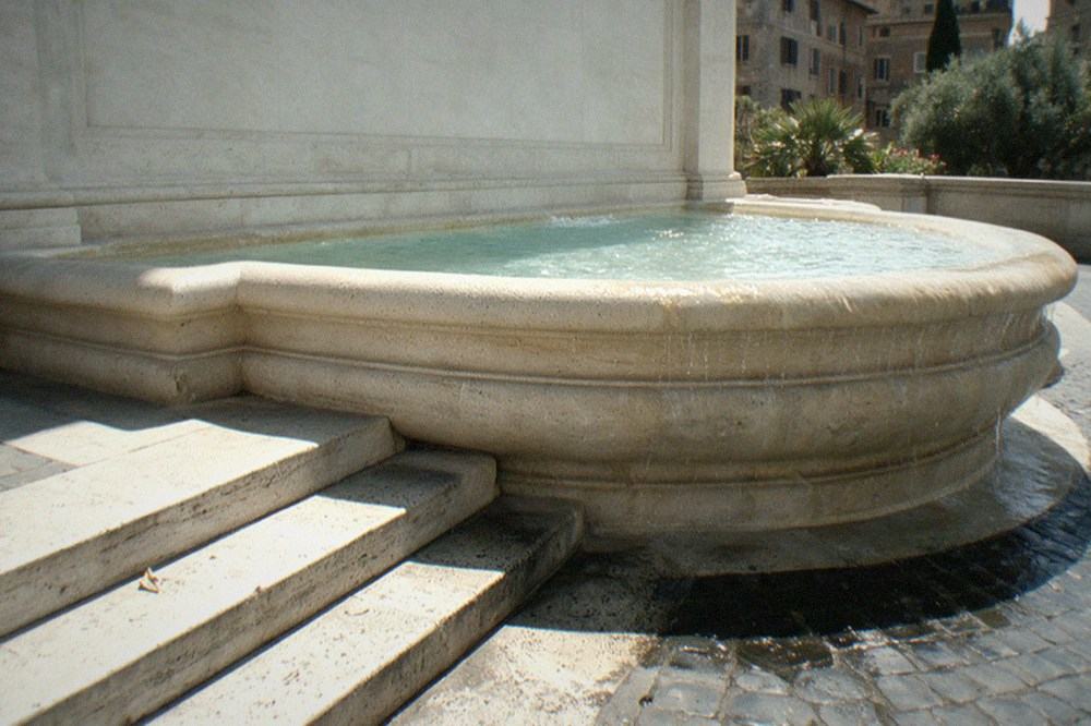 The low travertine steps beside the Trevi Fountain basin in bright midday sun