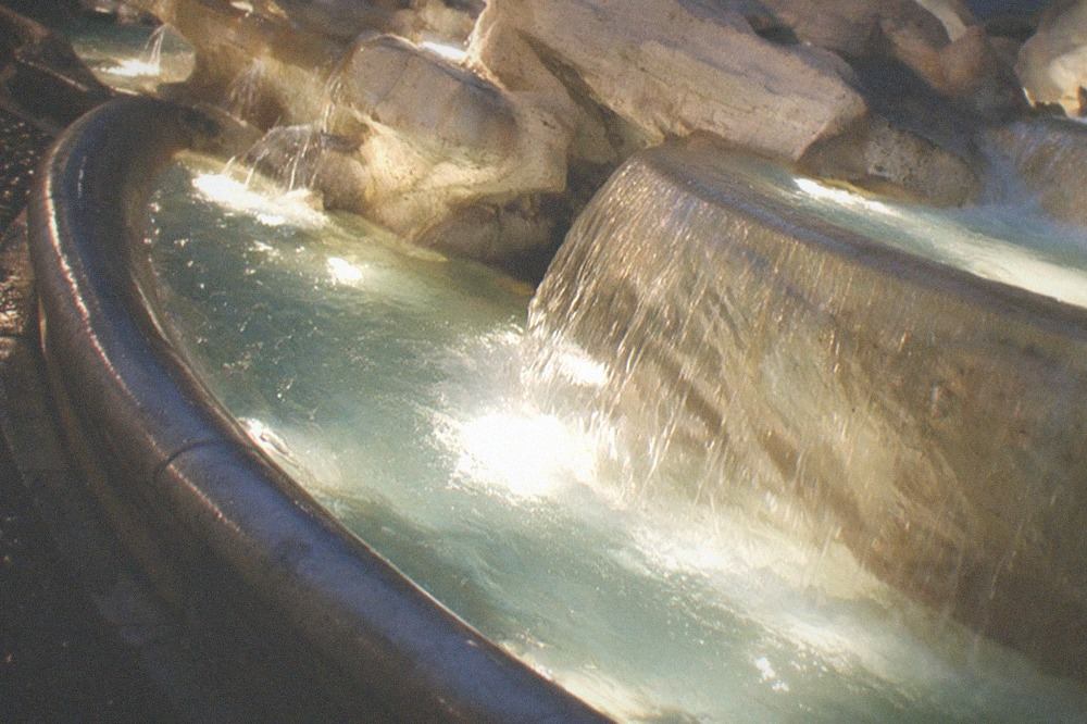 Water spilling over the Trevi Fountain travertine ledges into the floodlit basin at night