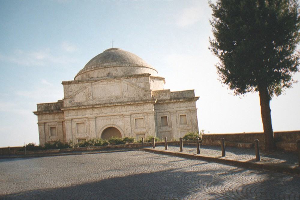 A small Roman piazza in the morning with a weathered travertine facade across the cobbles