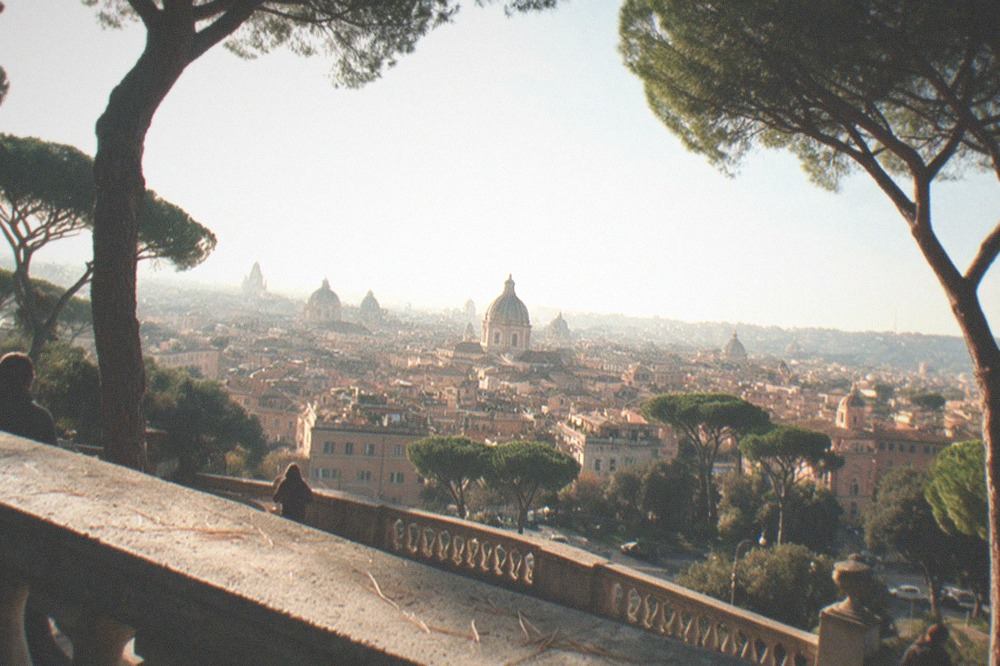 A panoramic view over Rome rooftops and domes from a green hilltop terrace