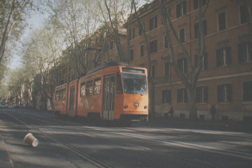 A Rome tram moving along a tree-lined street past old apartment buildings