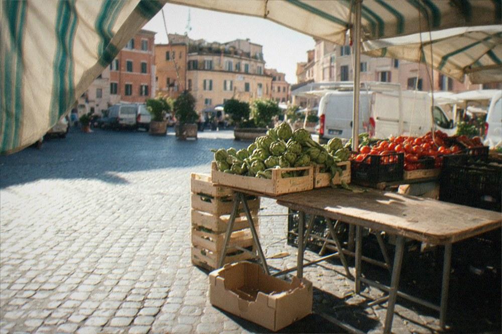 A Roman street market stall with fresh produce crates under awnings