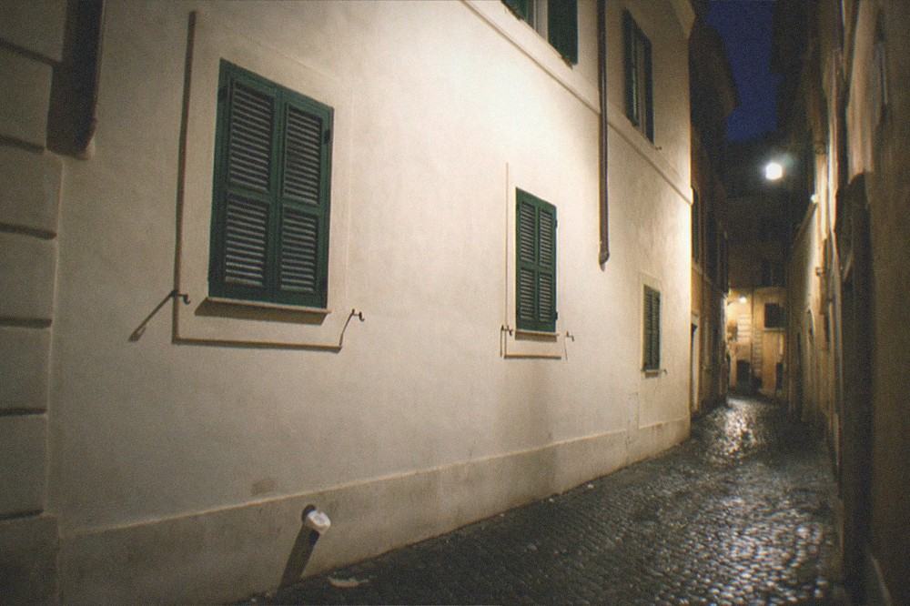 A Roman church facade and narrow lane illuminated by warm street lamps at night