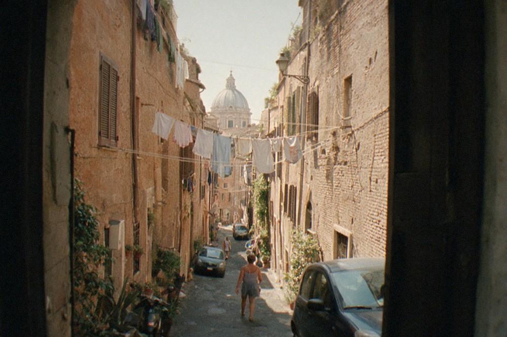 Narrow Roman street with warm stone buildings and a distant dome