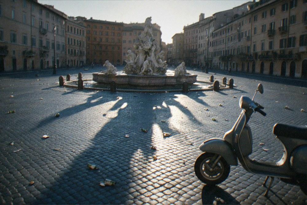 Empty Roman square at sunrise with long shadows across cobblestones